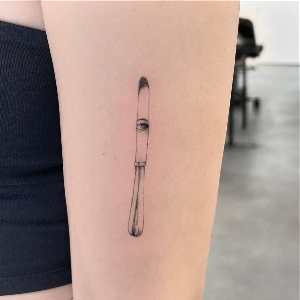 Illustrative style knife and eye tattoo located on the upper arm.