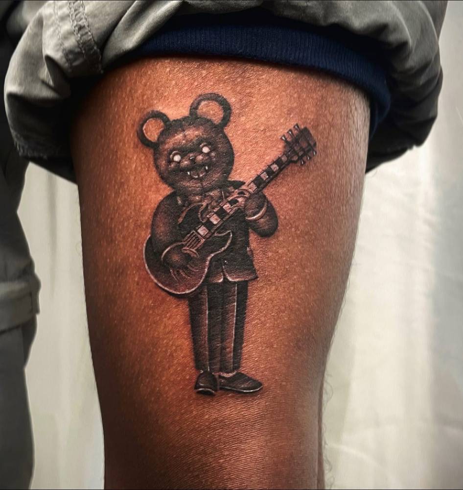 Guitarist teddy bear tattooed on the thigh, illustrative style.