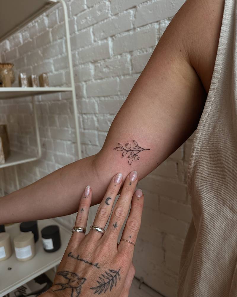 Blueberry branch tattooed on the inner forearm, done in fine line style.
