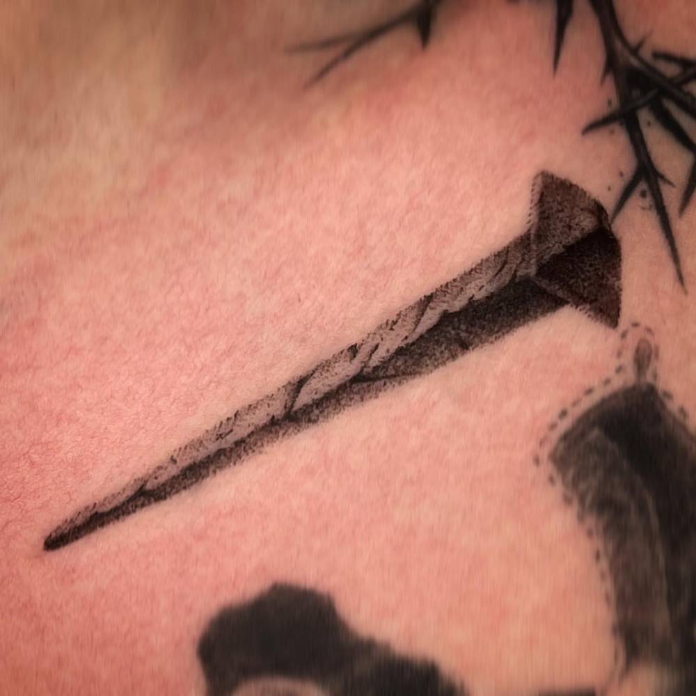 Nail tattoo in blackwork style located on the collarbone.