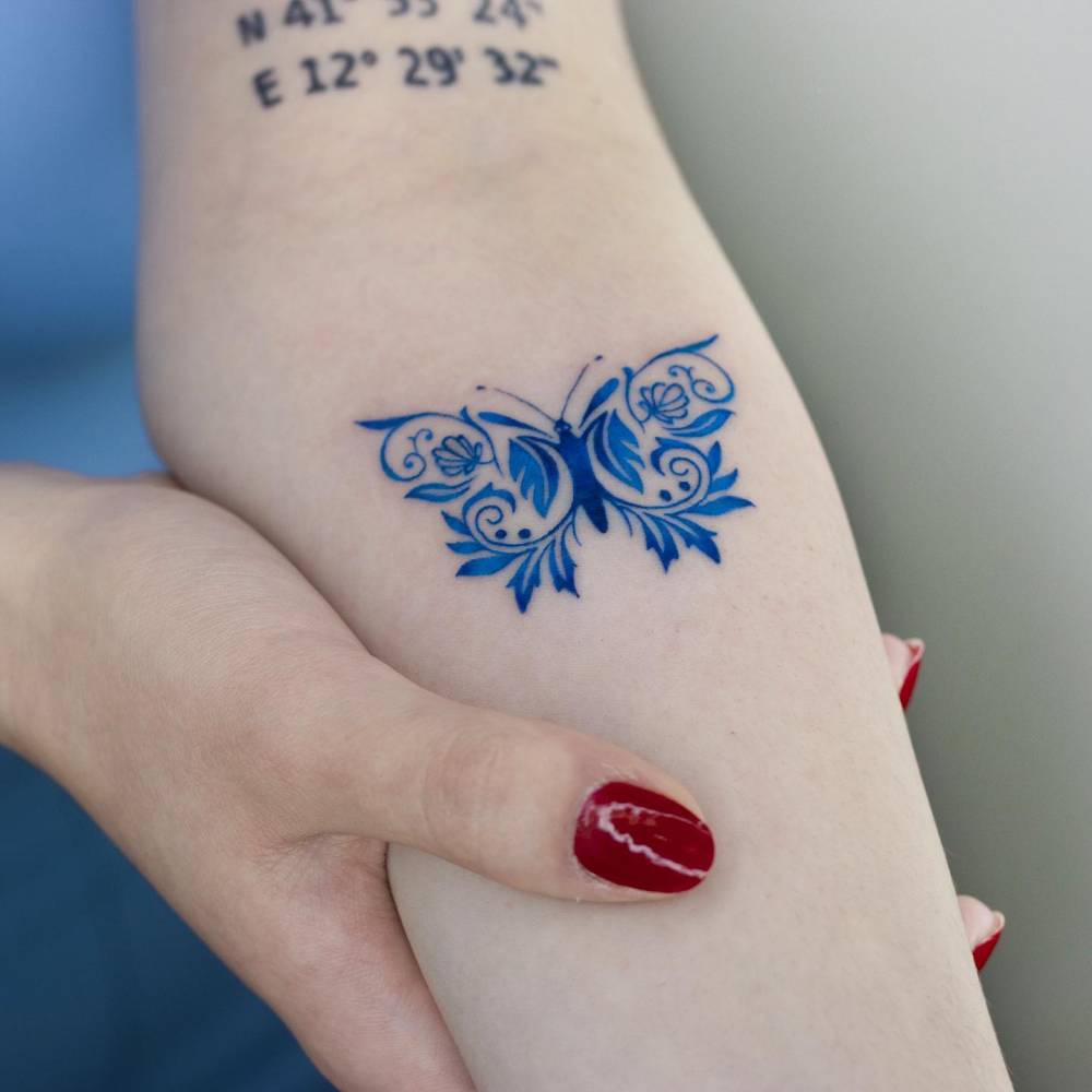 Illustrative style porcelain butterfly tattooed on the inner forearm.