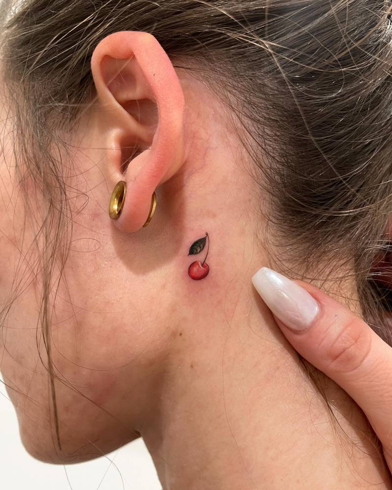 Watercolor style mini cherry tattoo done behind the ear.