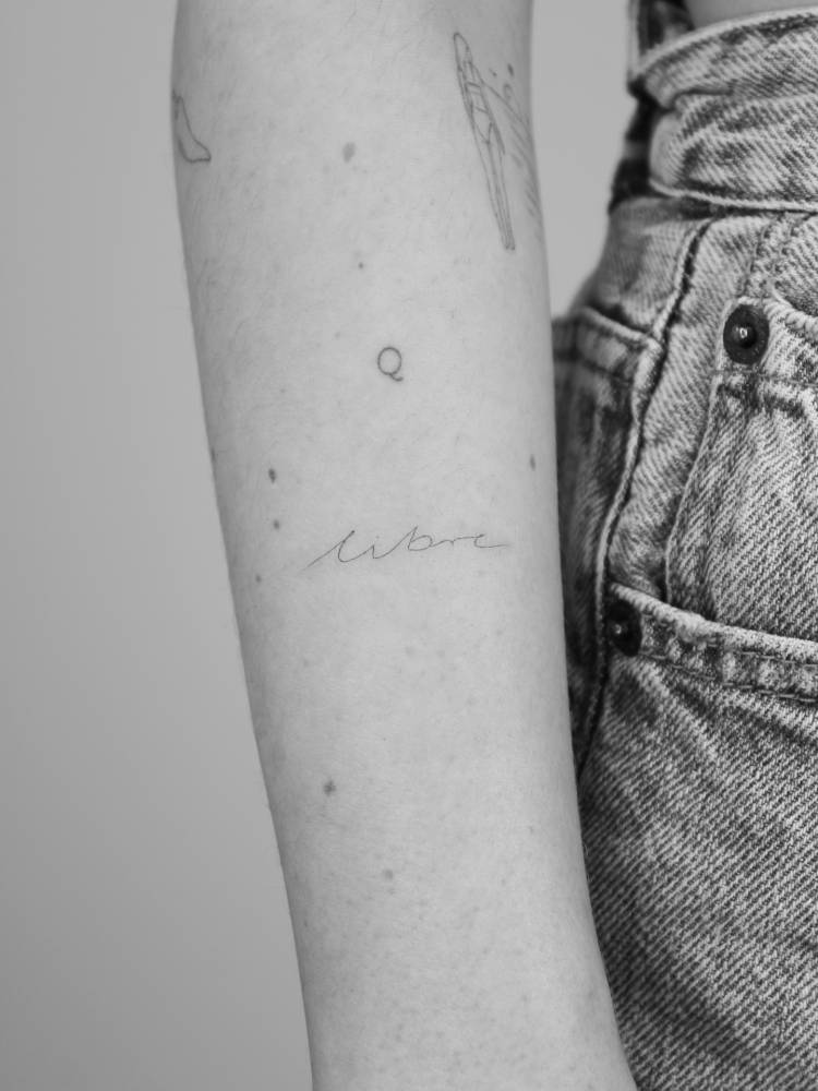 Handwritten lettering tattoo of the word "libre" placed on the forearm.