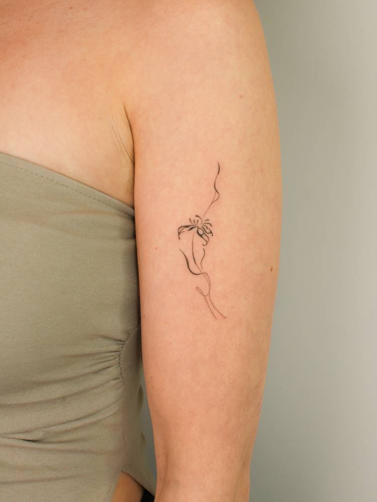 Fine line style ornamental flower tattoo placed on the upper arm.