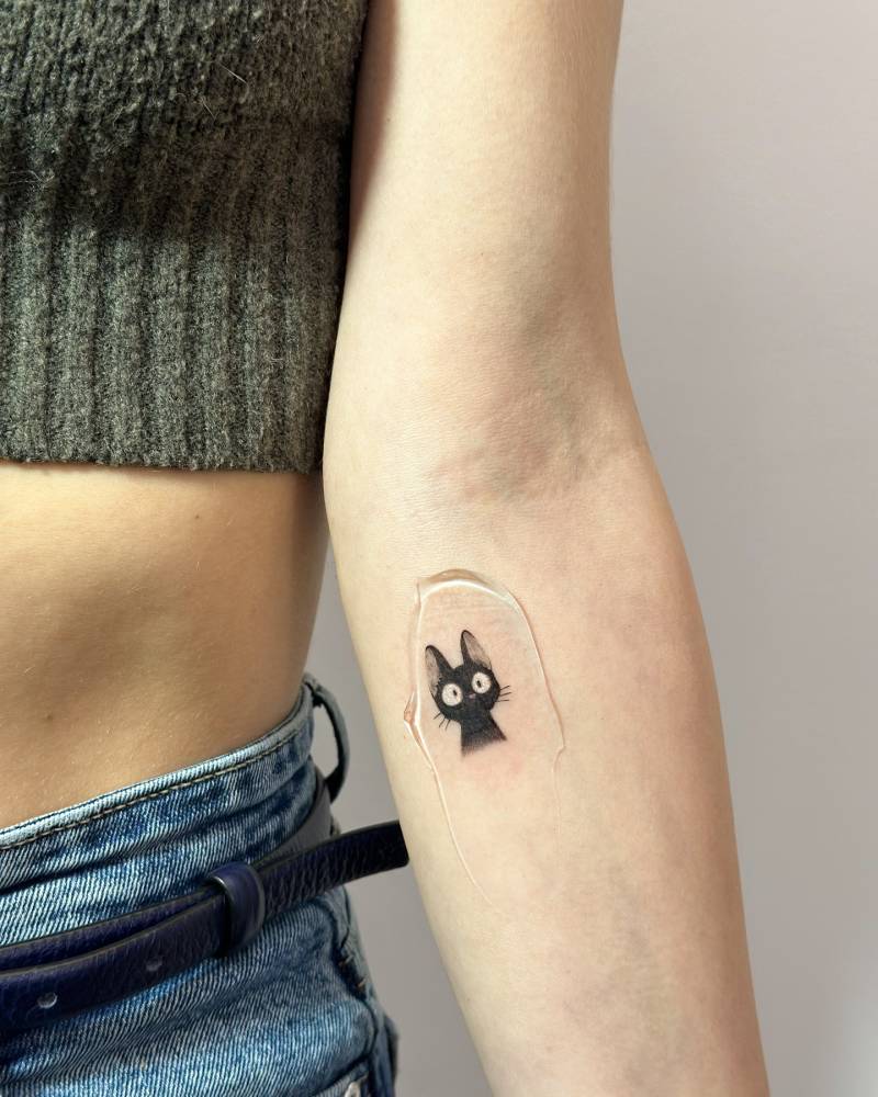 Jiji portrait tattoo in cartoon style located on the inner forearm.
