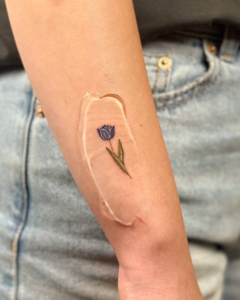 Watercolor style tulip tattoo located on the wrist.
