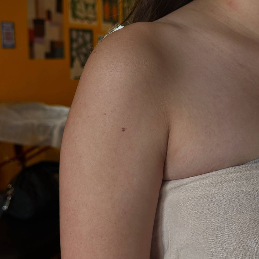 Tiny minimalistic paw freckle tattoo located on the upper arm.