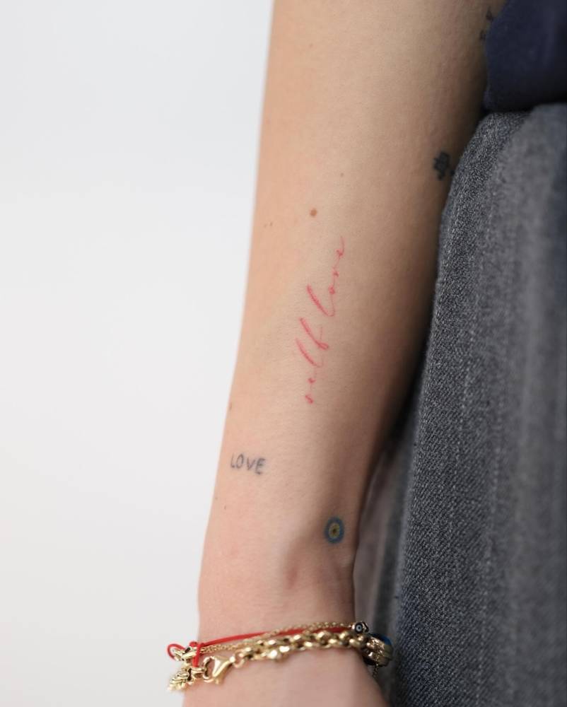 Healed "self love" lettering tattoo in red ink located on the wrist.