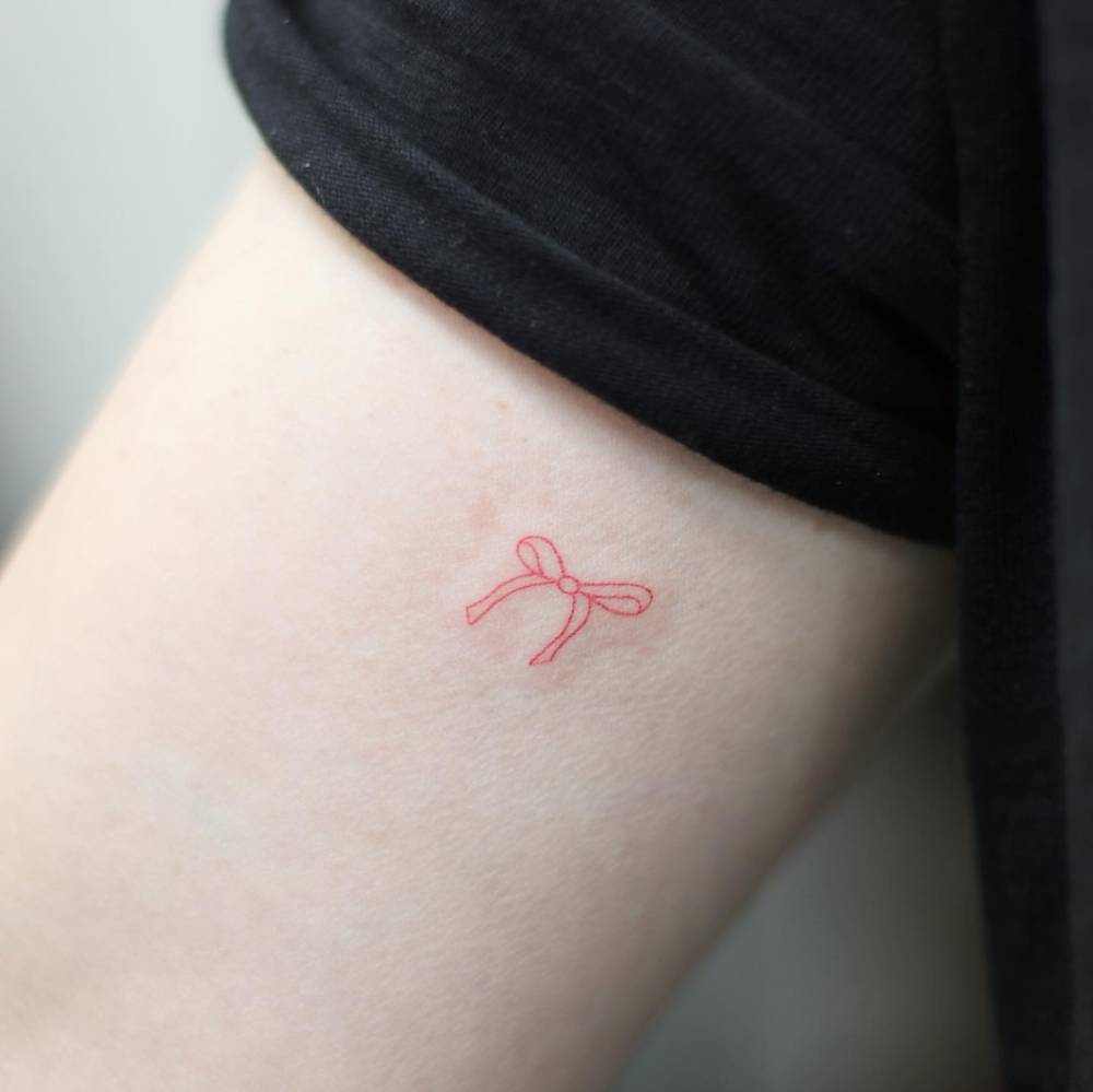 Tiny fine line red ribbon tattoo located on the inner arm.
