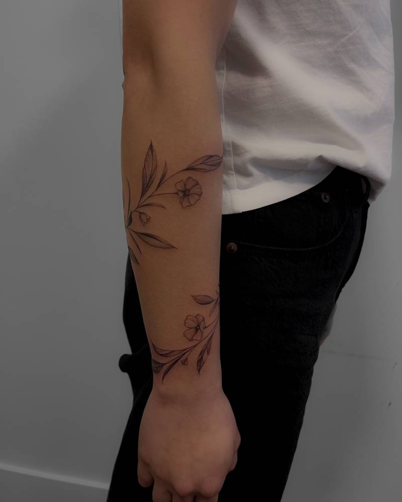 Illustrative style flower bracelet tattoo located on the forearm.