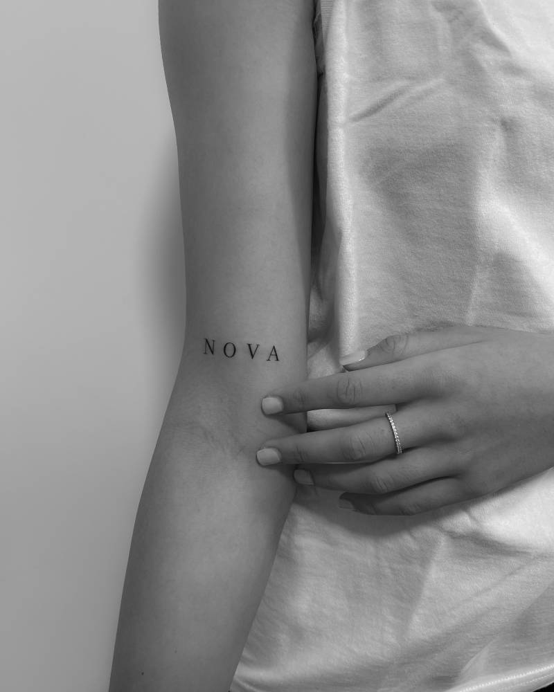 Serif font word "nova" tattooed on the bicep.