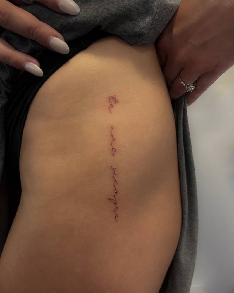 "Te amo siempre" lettering tattoo located on the hip.