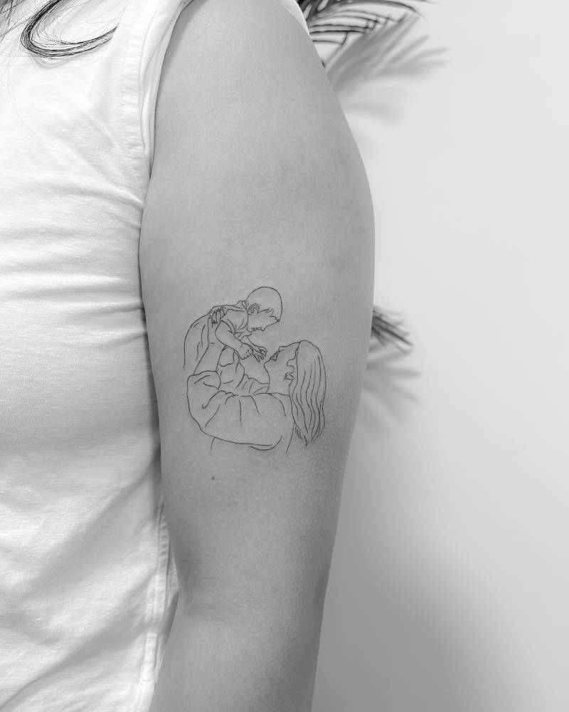 Motherhood tattoo located on the upper arm, done in fine line style.