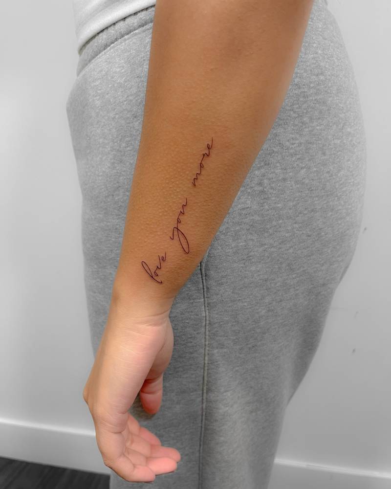 Handwritten lettering tattoo that says "love you more" placed on the wrist.