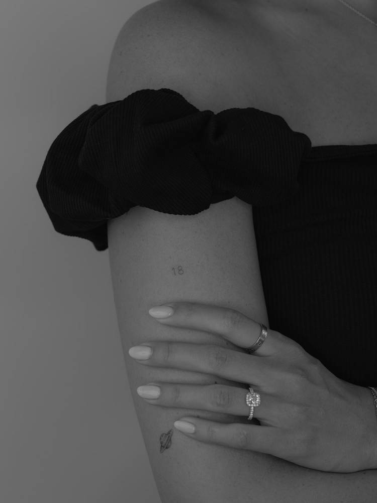Tiny lettering tattoo of the number "18" located on the upper arm.