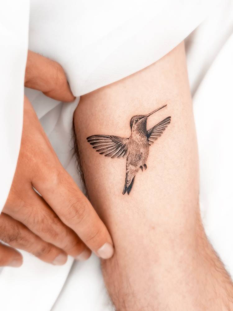 Micro-realistic style tattoo of a hummingbird located on the inner arm.