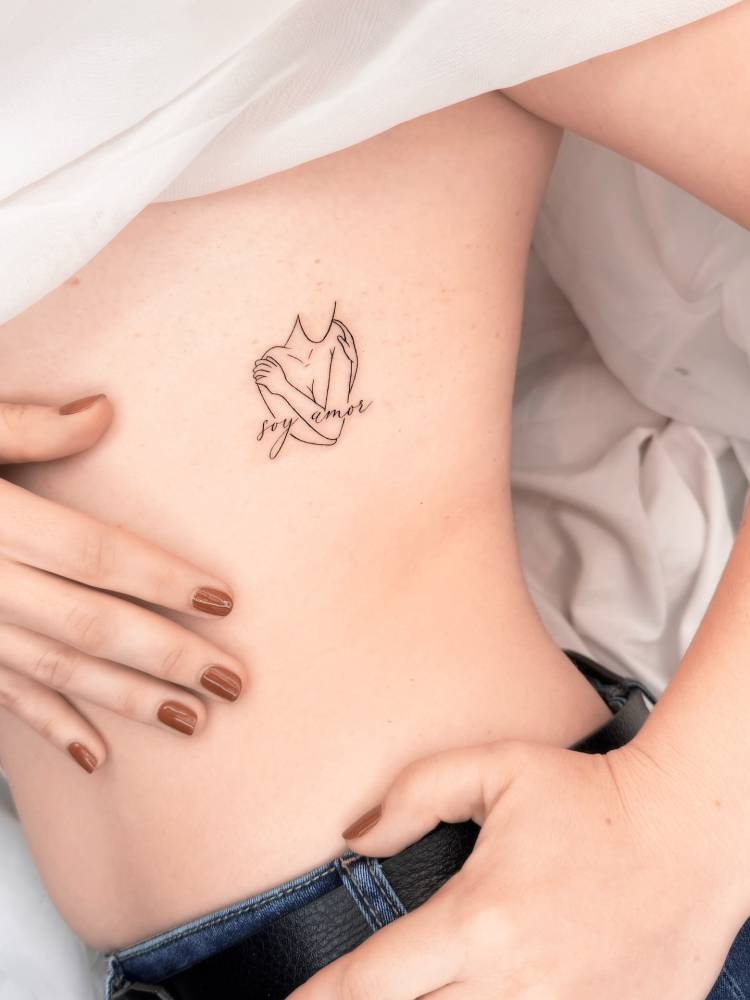 "Soy amor" and self hug tattoo located on the rib.