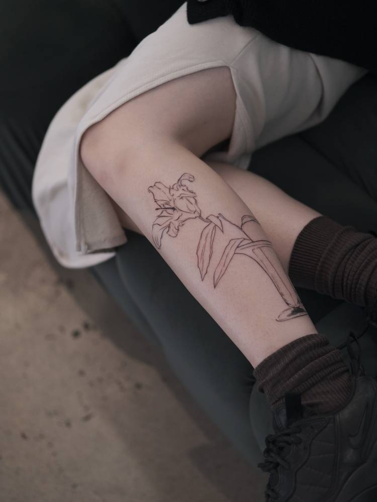 Line art style lily flower tattoo located on the shin.