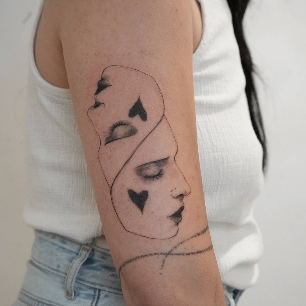 Illustrative style faces tattoo located on the upper arm.