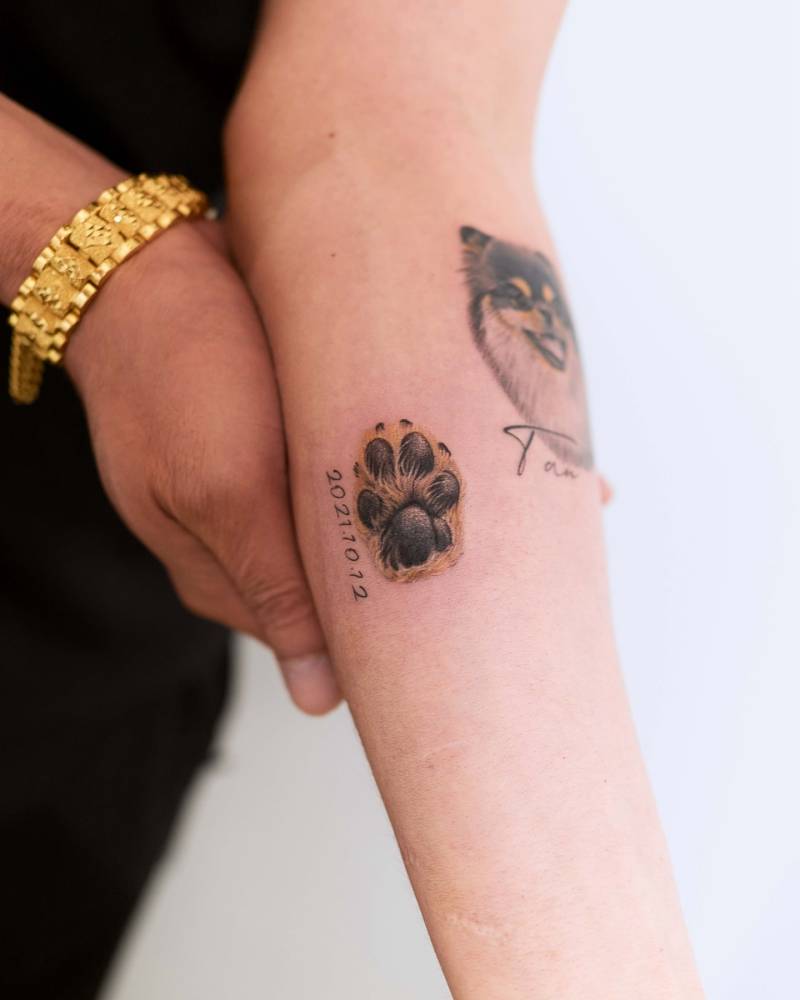 Dog paw and date tattoo located on the inner forearm.
