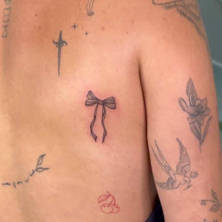 Illustrative style bow tattoo located on the shoulder blade.