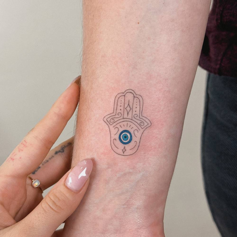 Hamsa tattoo in fine line style located on the wrist.