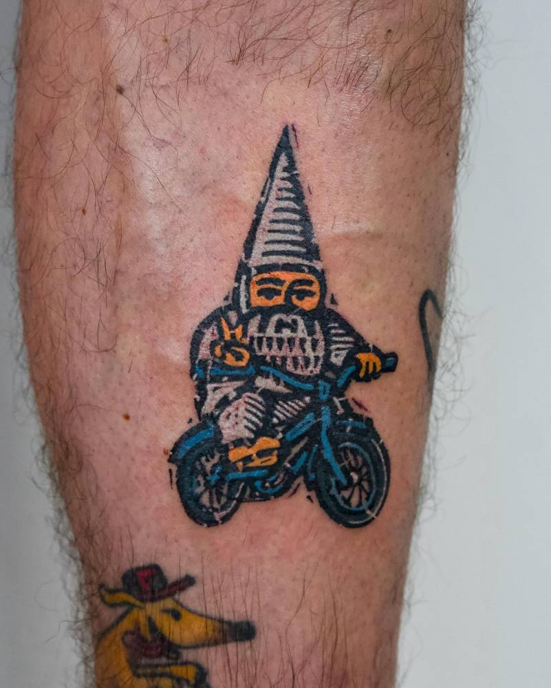 Cycling gnome tattoo located on the shin, pop art style.