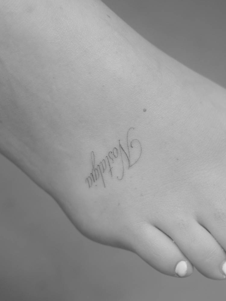 Script font word "nostalgia" tattooed on the foot.