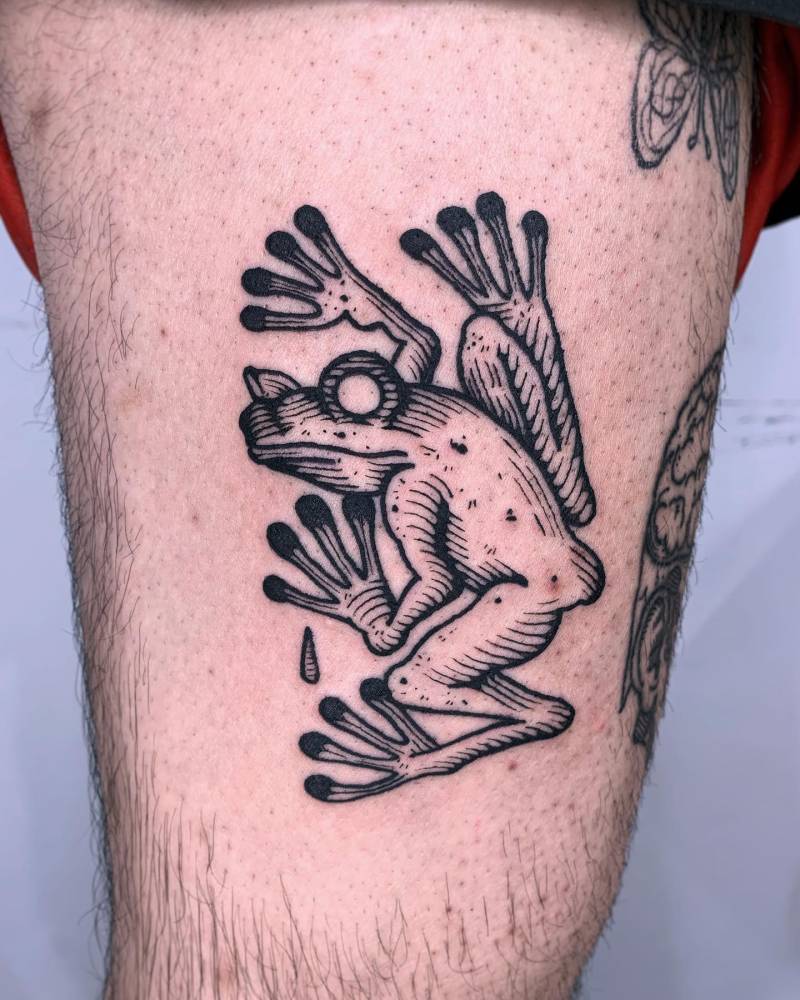 Frog tattoo located on the thigh, done in engraving style.