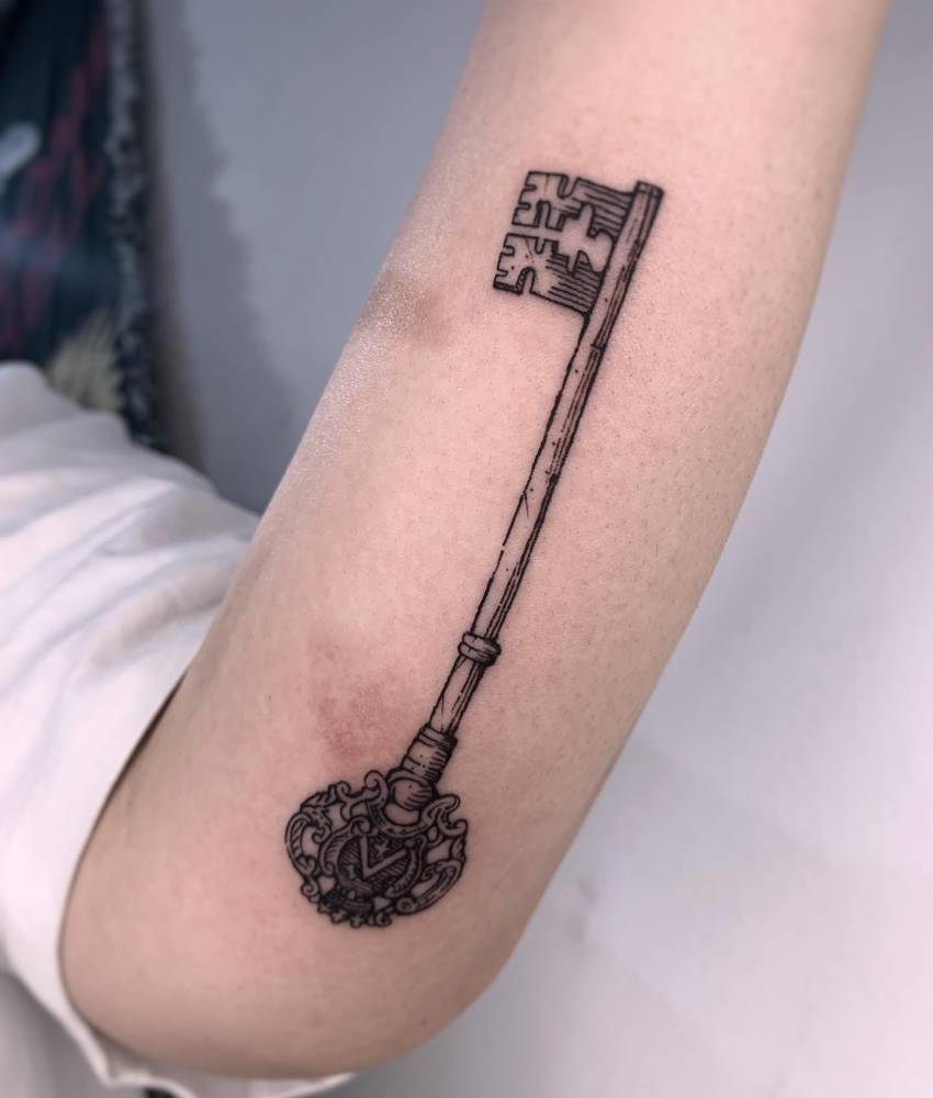 Engraving style key tattoo located on the inner forearm.