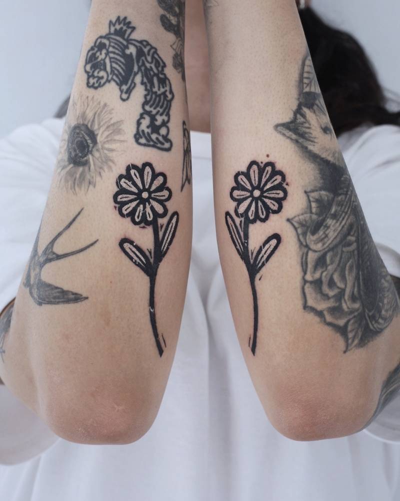 Individual matching pop art style daisies tattooed on the forearms.