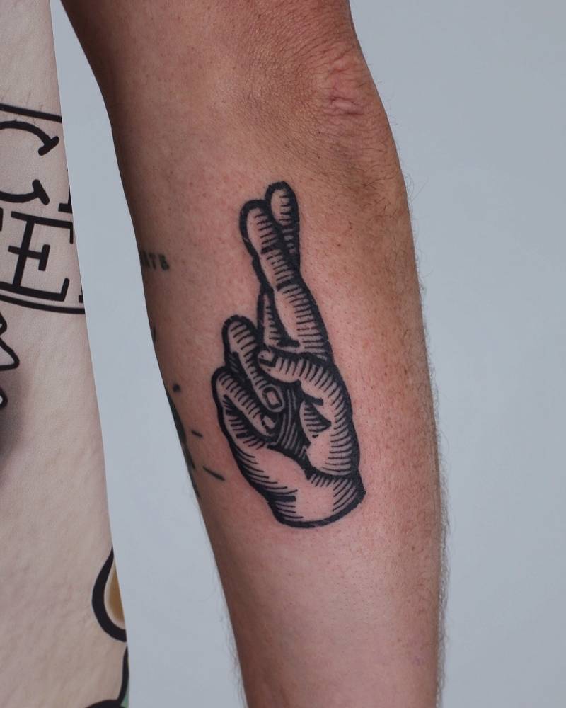 Crossed fingers in engraving style tattooed on the forearm.