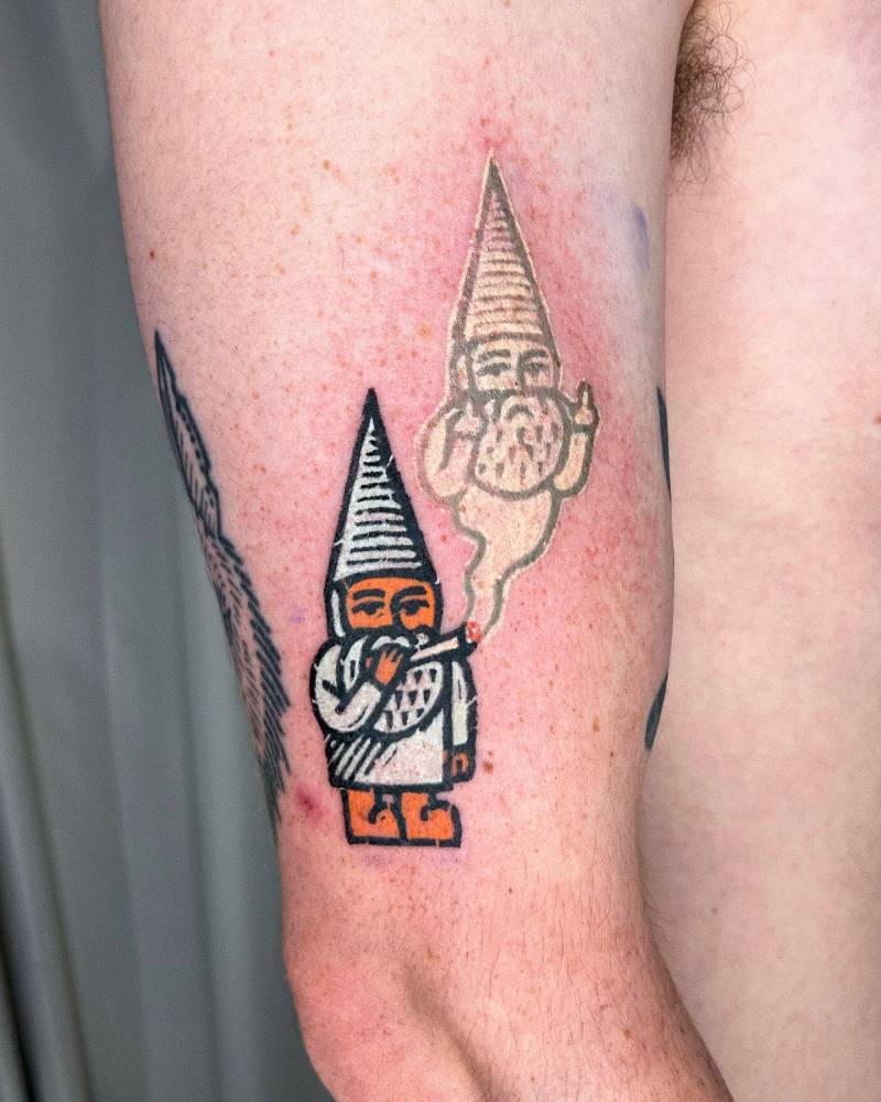 Pop art style smoking gnome tattoo located on the upper arm.