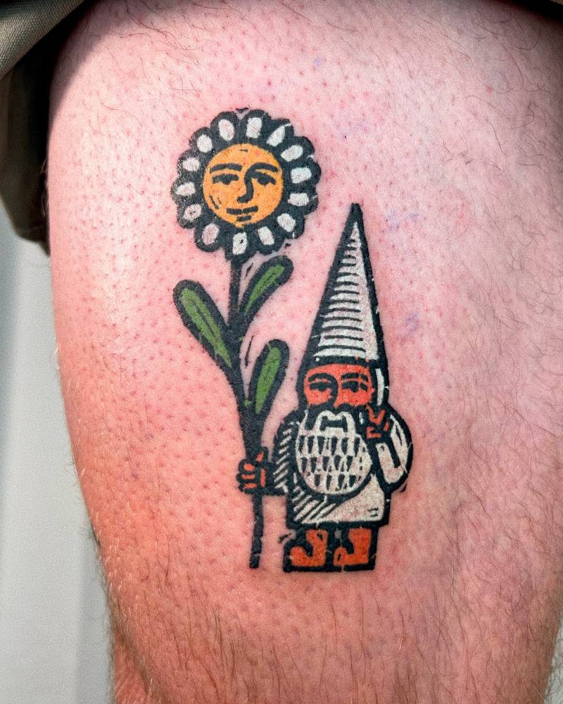 Gnome holding a daisy flower tattooed on the thigh.