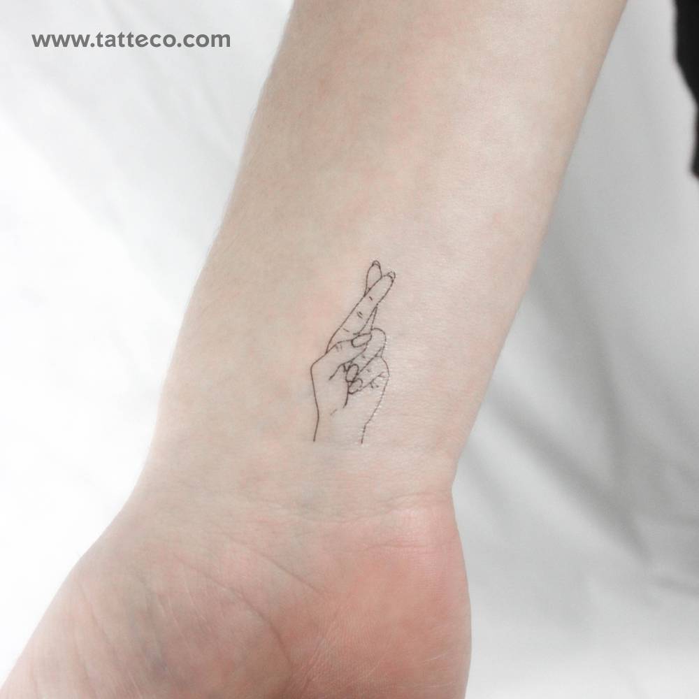 Fine line style crossed fingers temporary tattoo located on the wrist.