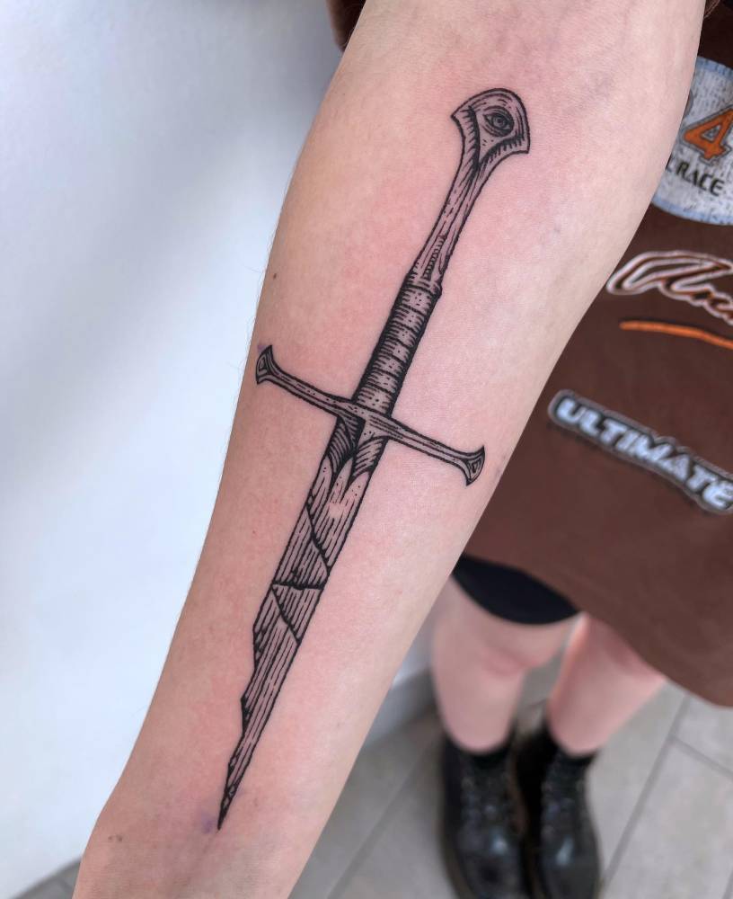 Engraving style broken sword tattoo located on the inner forearm.