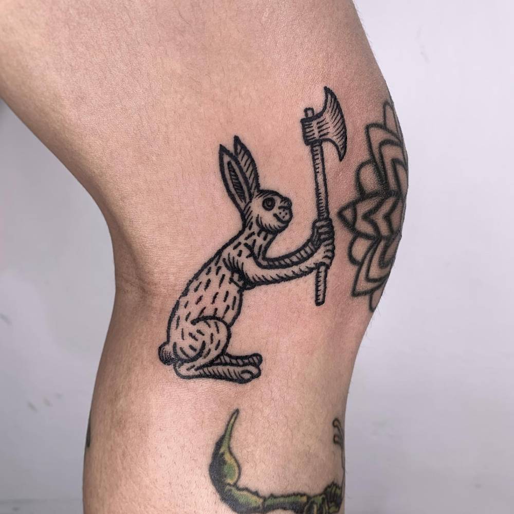 Engraving style hare and axe tattoo located on the knee.