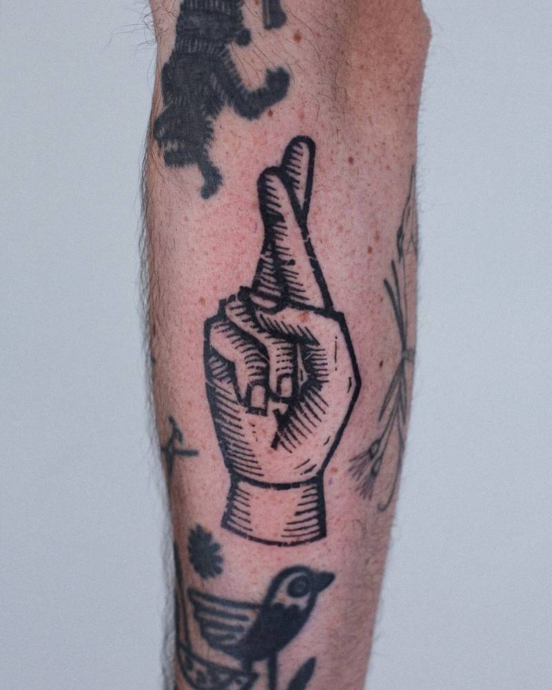 Crossed fingers in engraving style tattooed on the forearm.
