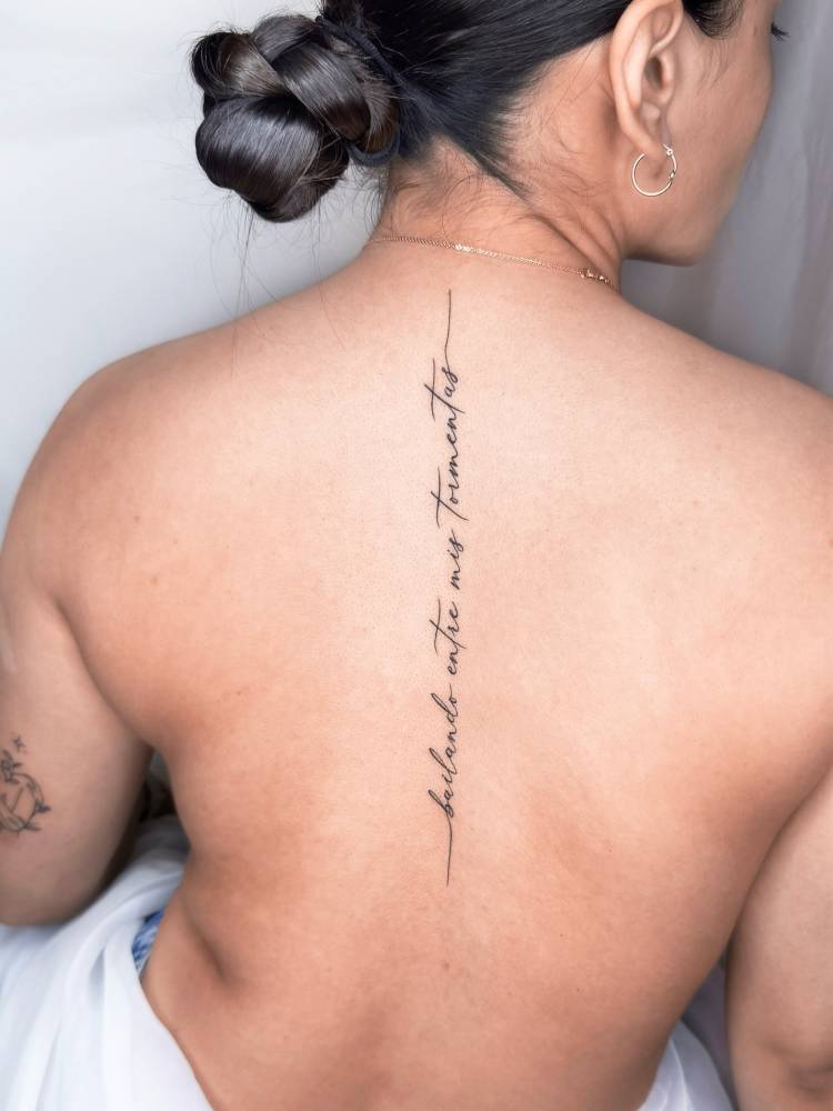 "Bailando entre mis tormentas" lettering tattoo placed on the spine.