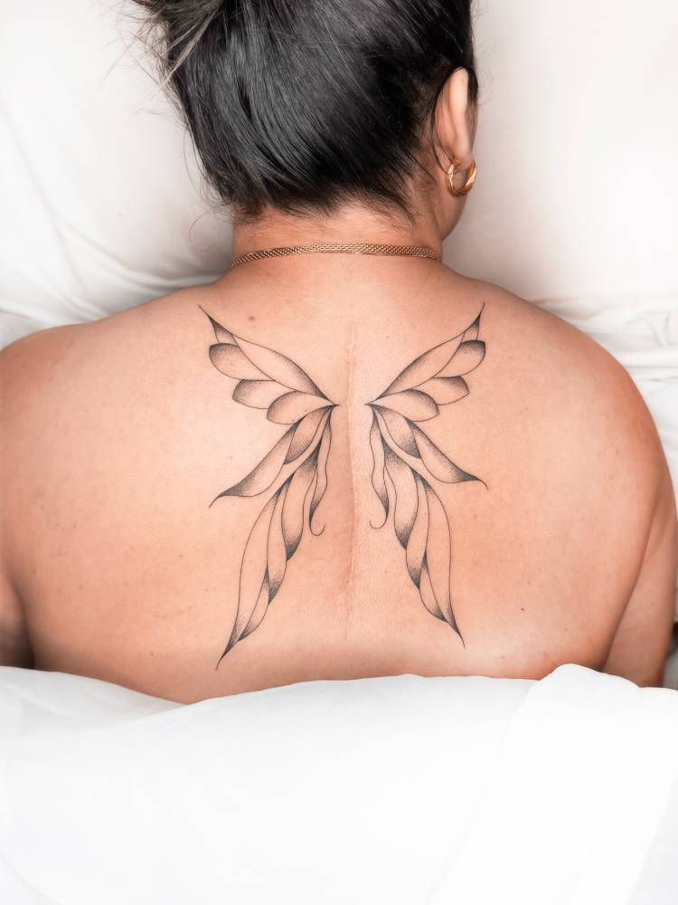 Illustrative style butterfly wings scar cover up tattoo located on the back.