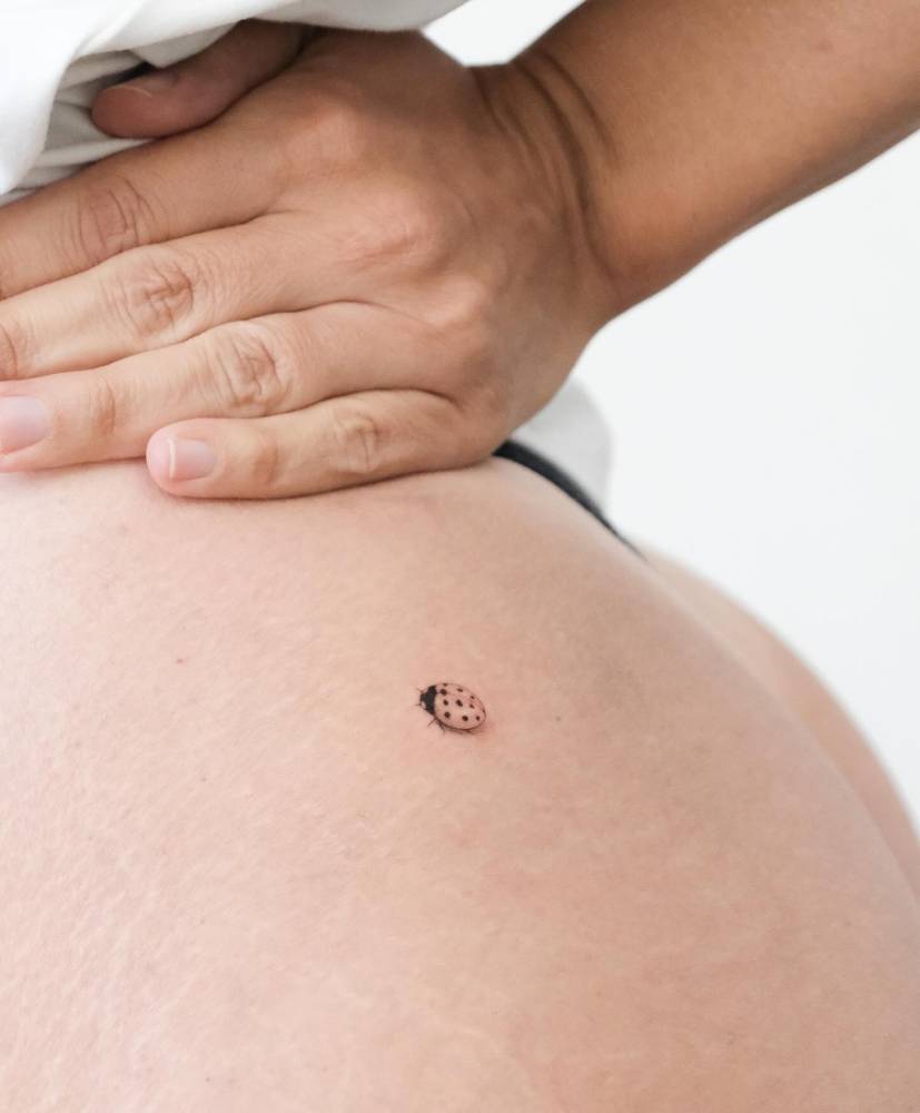Single needle ladybug tattoo placed on the butt cheek.