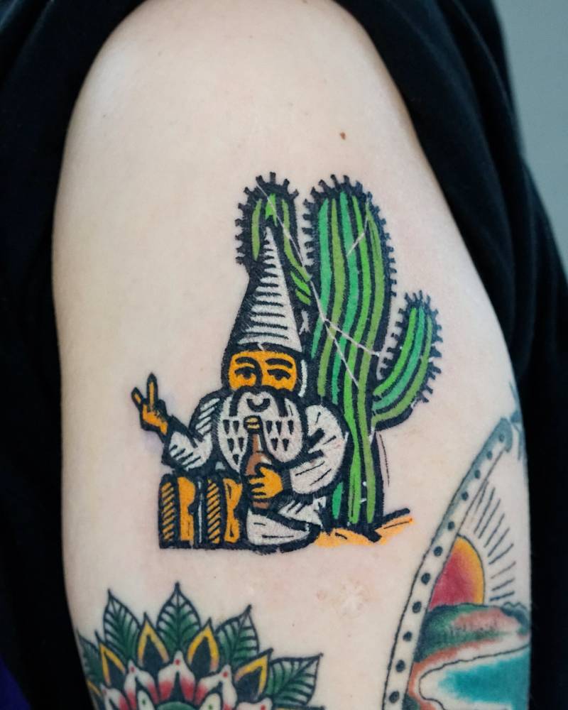 Gnome and saguaro tattoo in pop art style located on the upper arm.