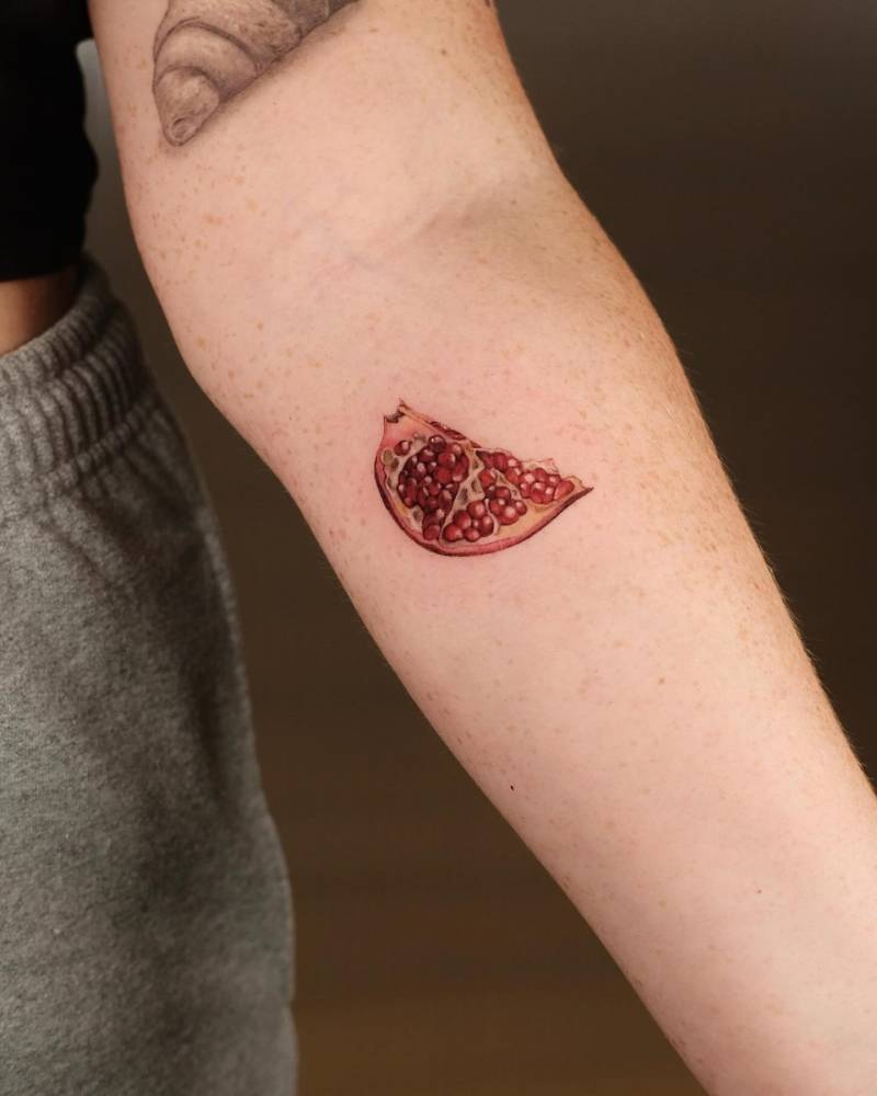 Micro-realistic pomegranate tattoo located on the inner forearm.