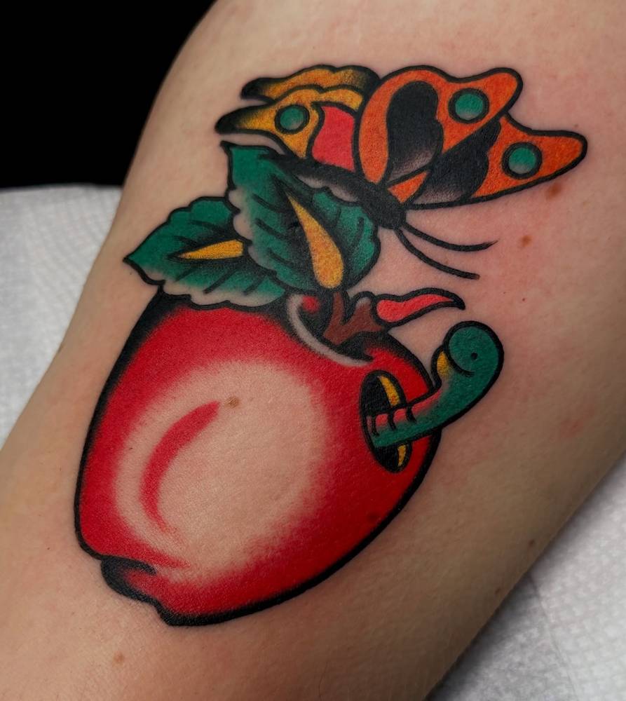 Apple and butterfly tattoo in traditional style located on the thigh.