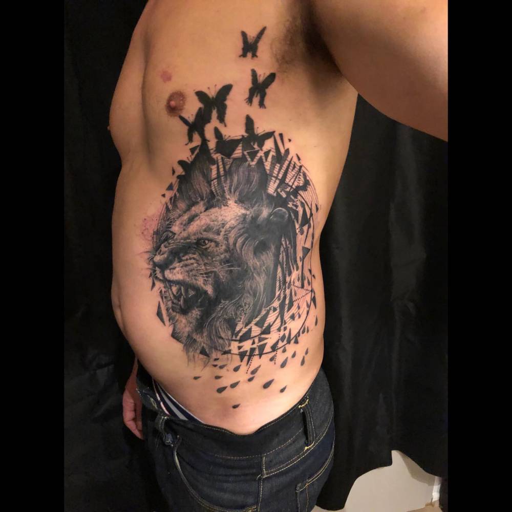 Black and grey style lion portrait tattoo located on the rib.