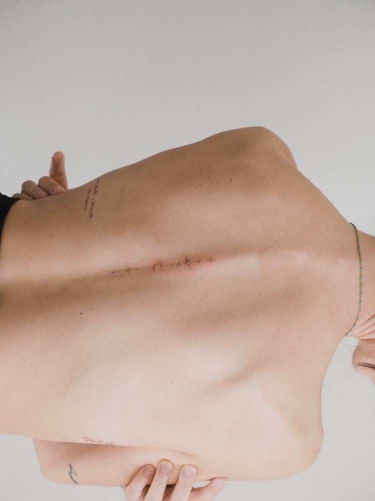Fine line style symbol chain tattoo located on the spine.