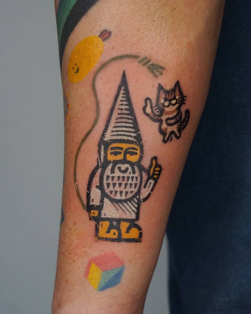 Pop art style gnome and cat tattoo located on the inner forearm.