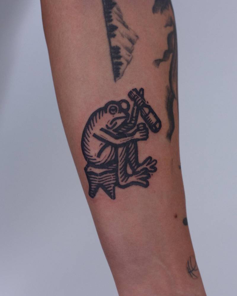 Drinking frog tattoo in blackwork style located on the inner forearm.
