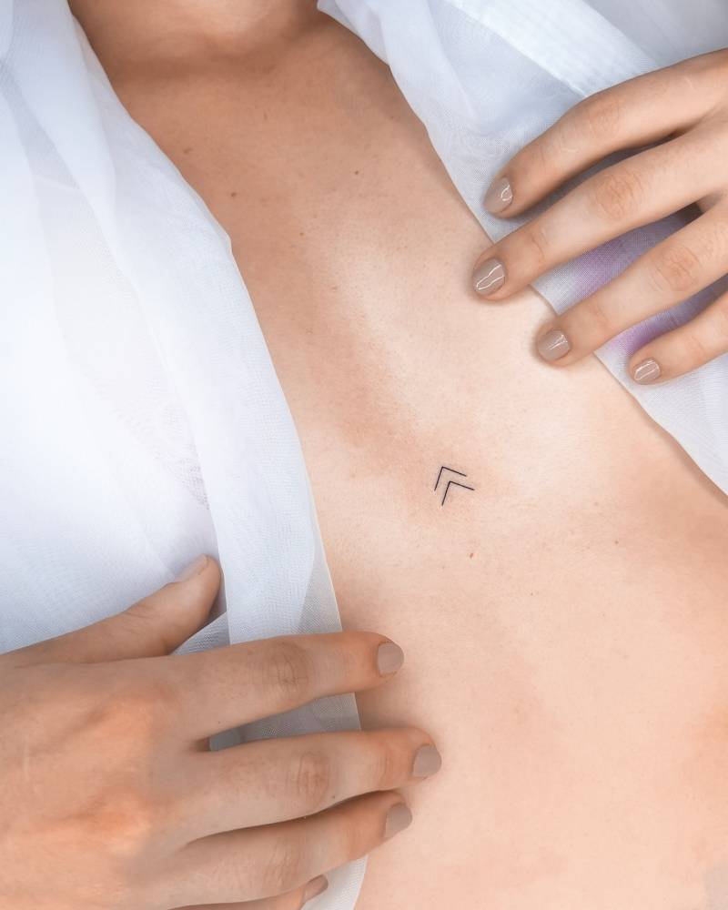 Chevron symbol tattooed on the sternum, minimalistic style.