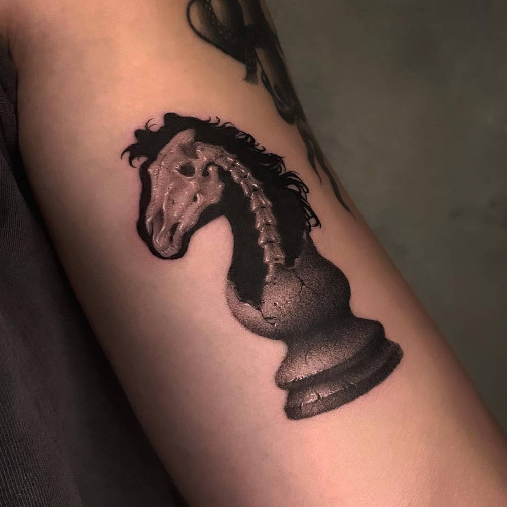 Broken chess knight piece tattooed on the bicep.